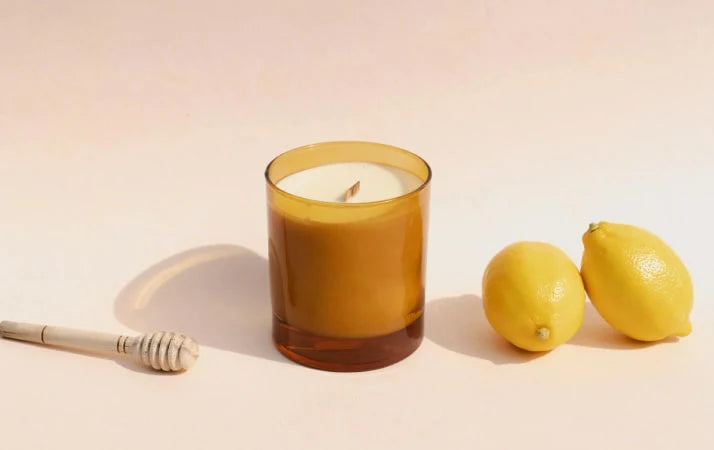 Bougie parfumée dans un verre ambré avec deux citrons et une cuillère à miel, ambiance détente.